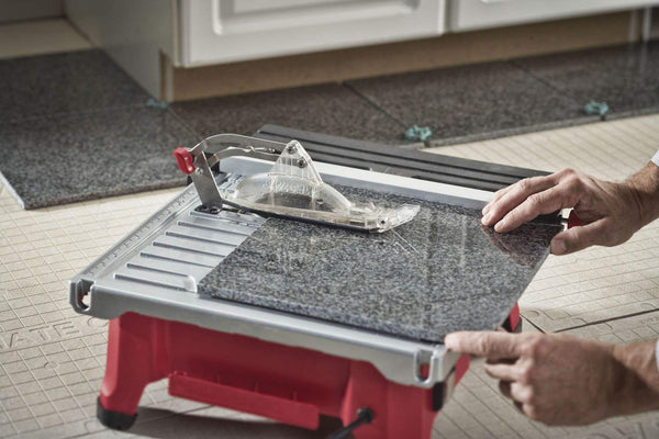 Person uses a manual tile cutter to score a dark granite floor tile on a portable cutting table
