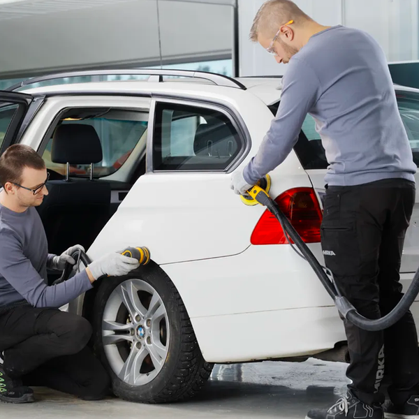 Two automotive technicians in safety glasses work on a white SUV with tools in a workshop