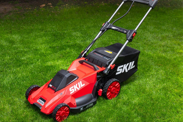 Red SKIL lawn mower on a green lawn with a black grass bag attached.