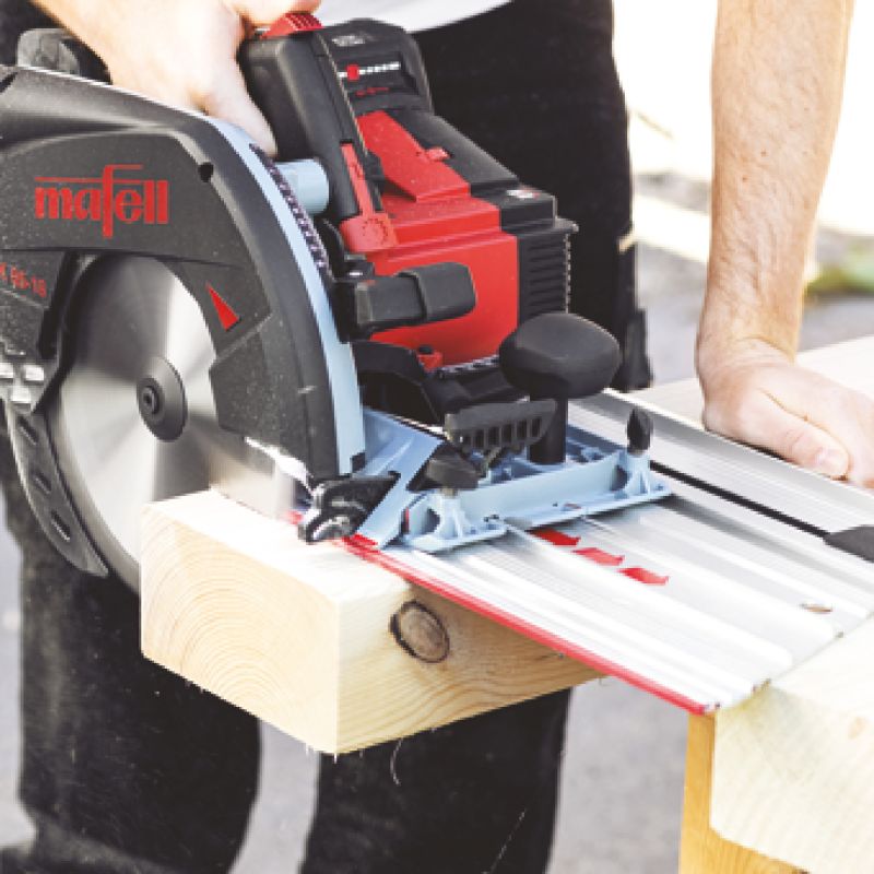 Mafell circular saw on a silver guide track cutting a wooden beam with a hand guiding.