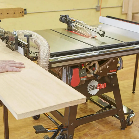 Table saw with a person's hand on a piece of wood in a workshop setting
