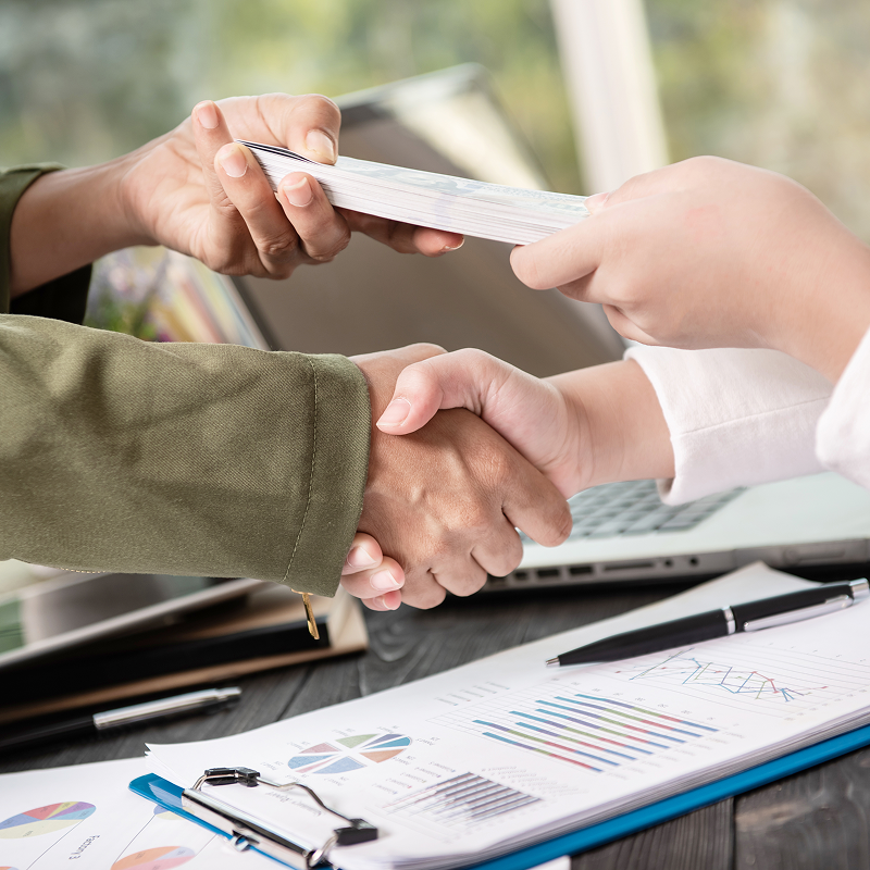 Two people shaking hands with a laptop and documents in the background