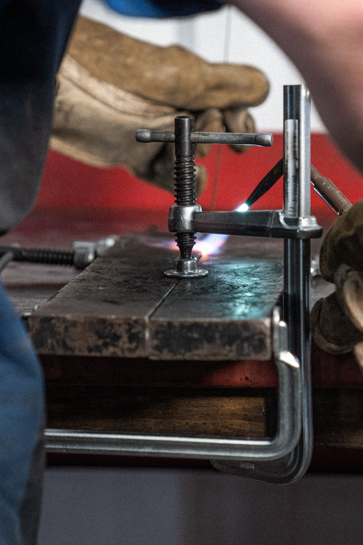 Close up of a Bessey all steel F-Style welding clamp with a T handle on a workbench