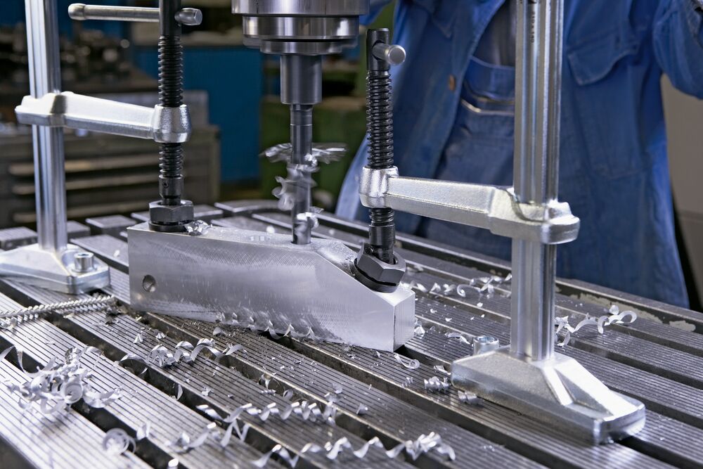 Two table mount hold down clamps securing a metal block on a milling machine table.