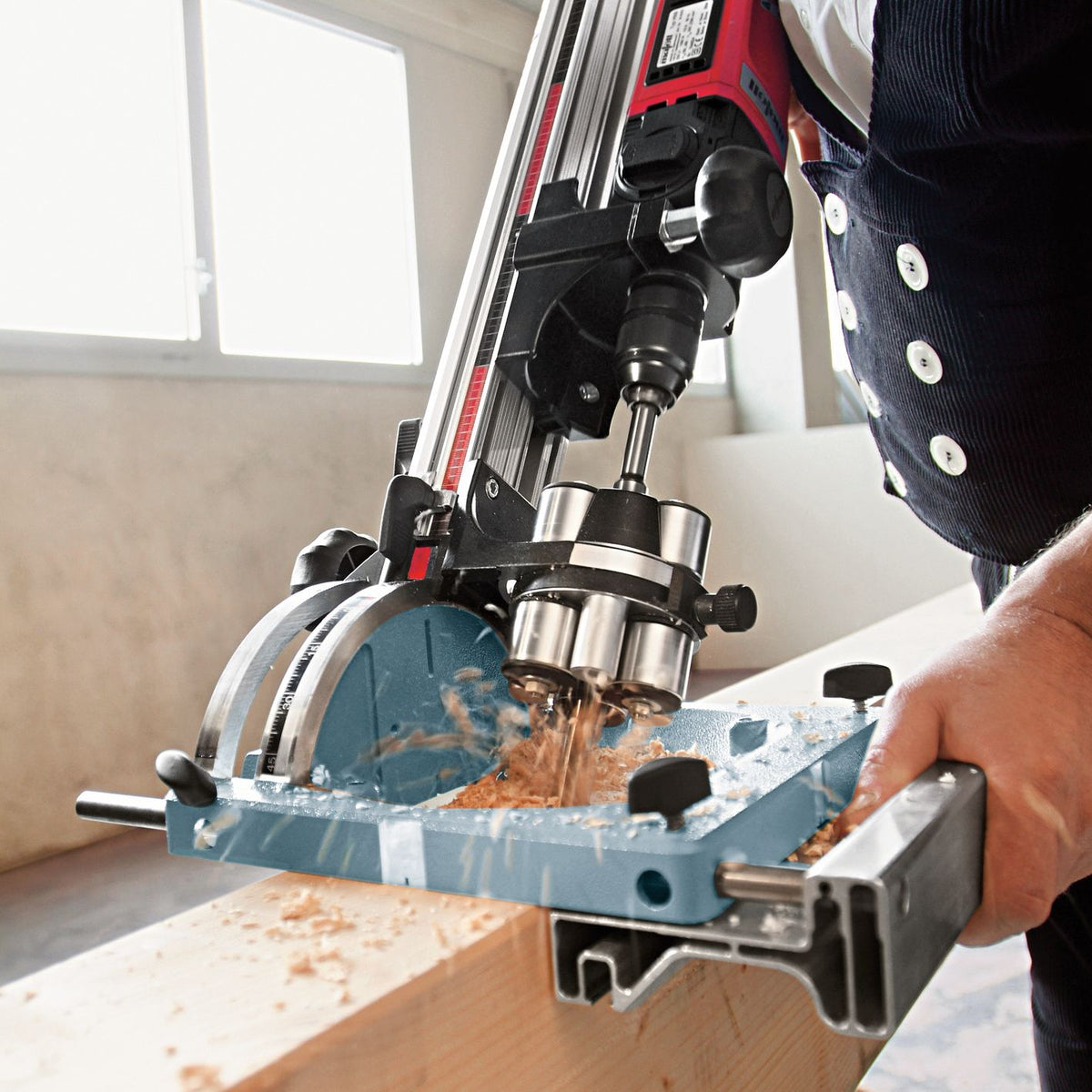 Operator uses the parallel guide fence on a BST drilling station to bore into wood, producing wood shavings