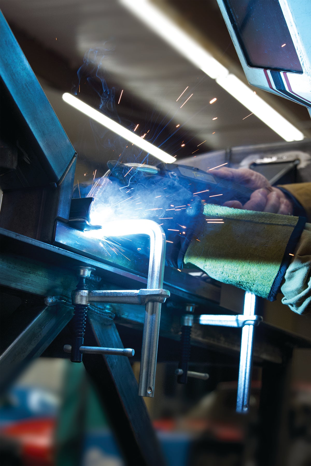 Welding arc with sparks flying as a Bessey clamp holds metal in a busy shop