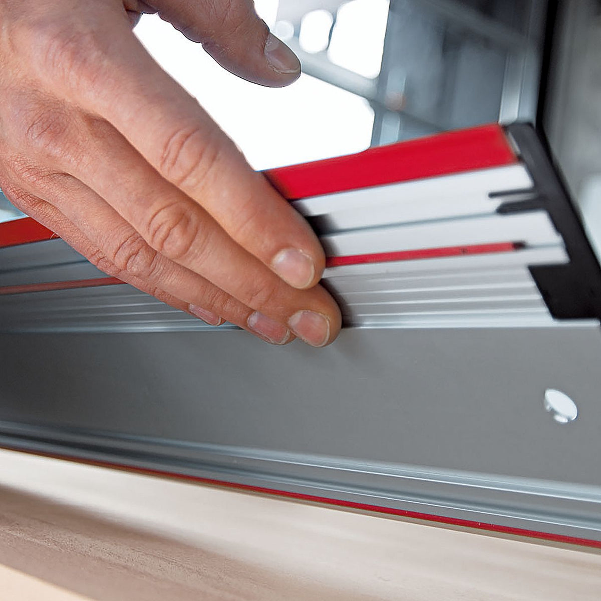 Hand slides the guide rail along the aluminum track marked with red Mafell branding beside a wood panel