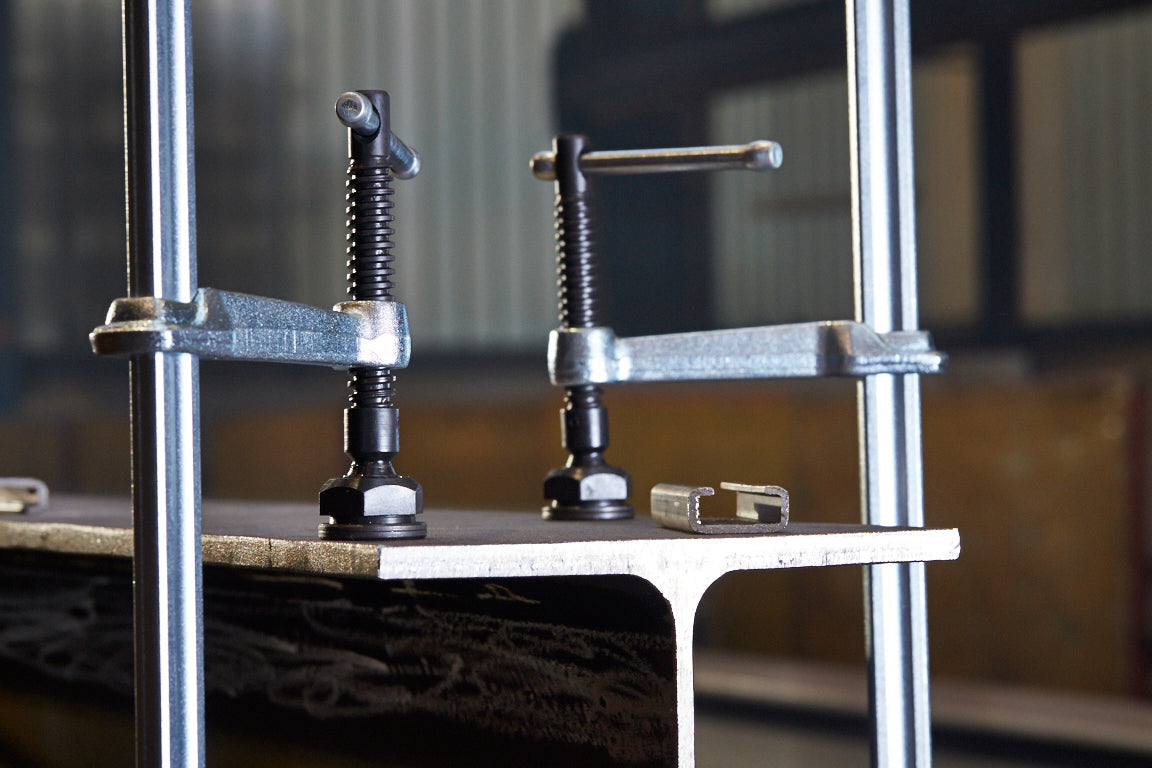 Two all-steel F-style welding clamps mounted on a frame with a worker in the background