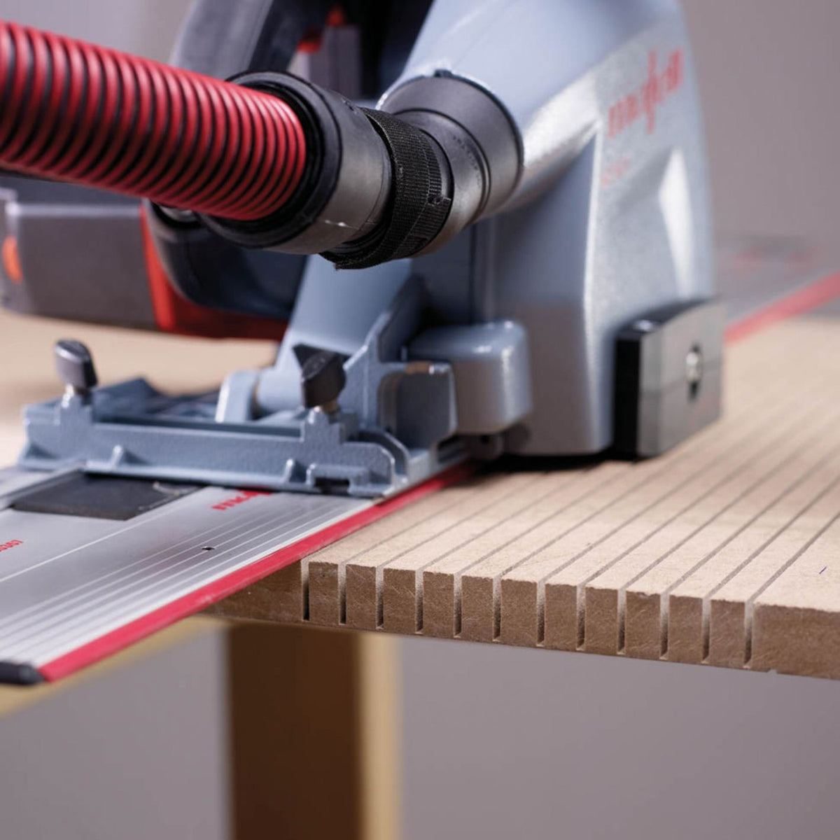 Mafell track saw cutting a grooved wooden panel along a red guide rail.