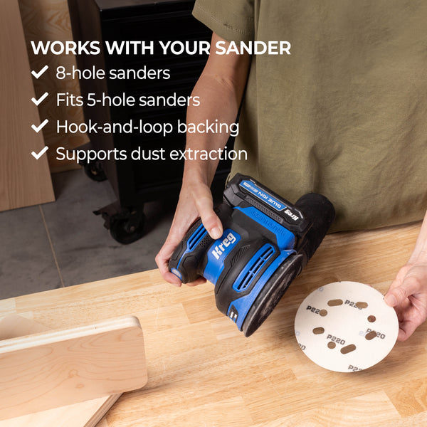 Person uses blue Kreg sander on a wooden surface with a sanding disc nearby