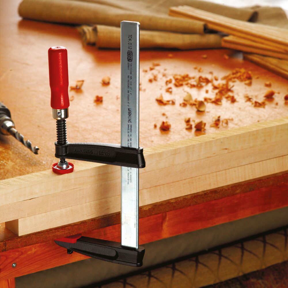 Bessey flat rail woodworking F style clamp with red handle securing a board on a workbench