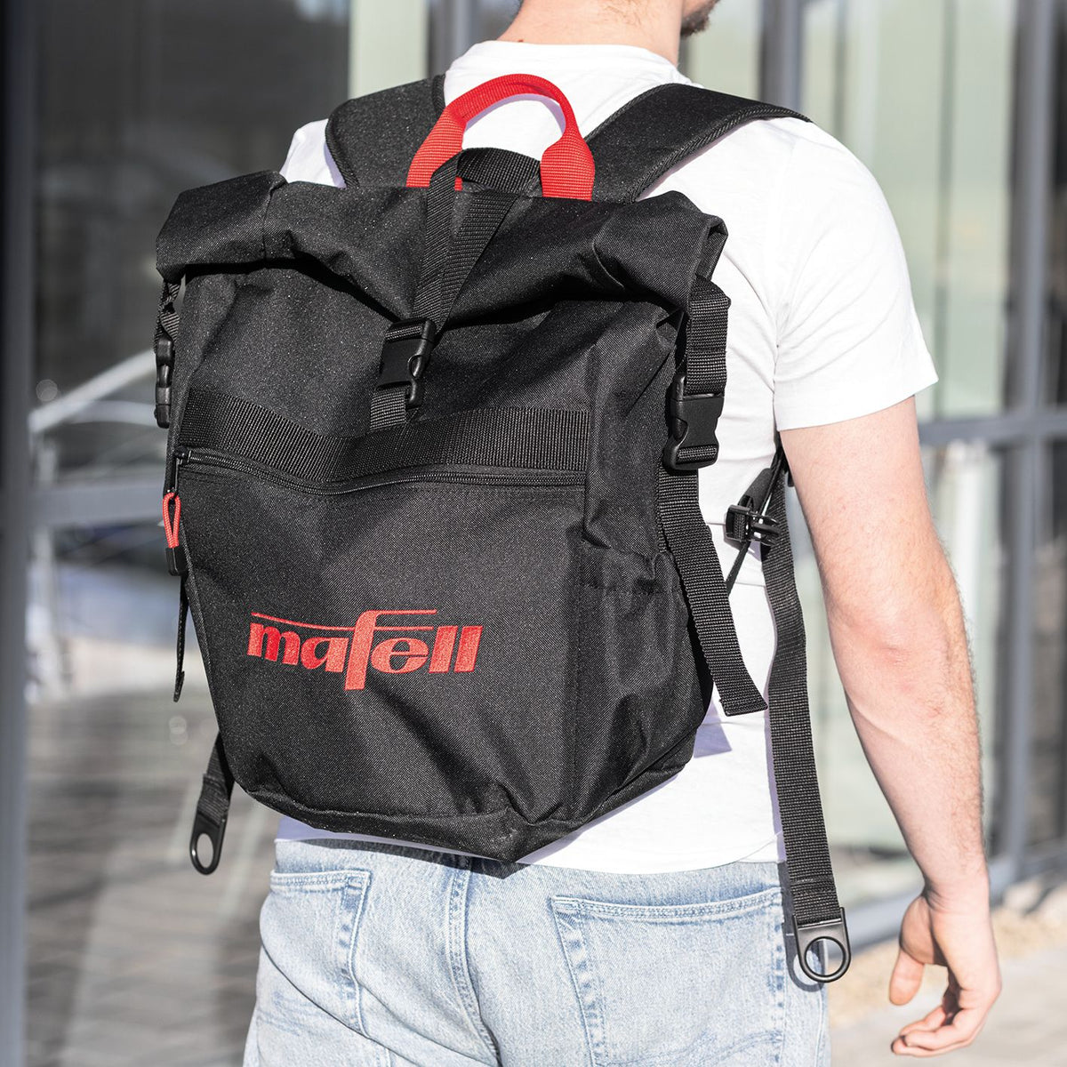 Back view of a black Mafell roll-top backpack worn by a person with a red handle and Mafell logo