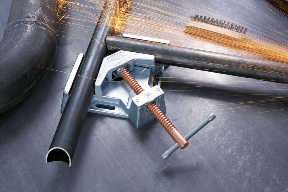 Welding angle clamp mounted on a steel pipe with copper spindle as sparks fly in the background
