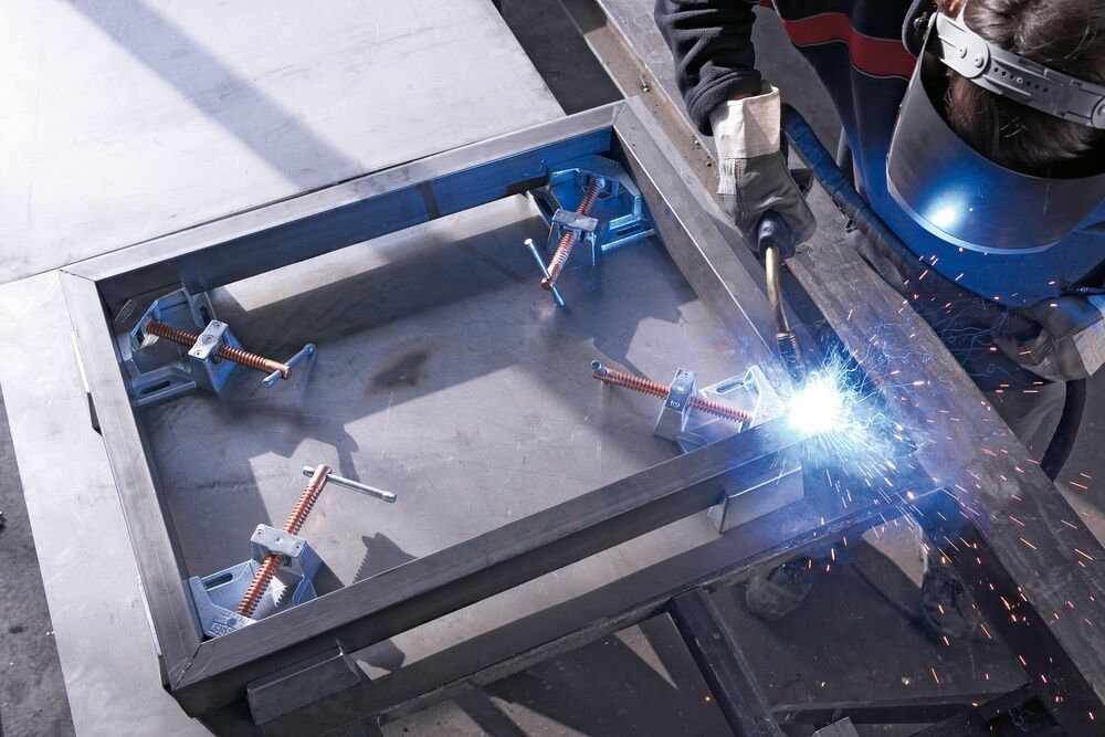Welder in protective gear uses multiple welding clamps to assemble a steel frame